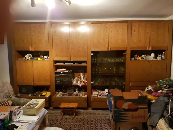 Großer Wohnzimmerschrank aus Holz mit Glastüren, Dekoration, Kartons und Bücherstapel.