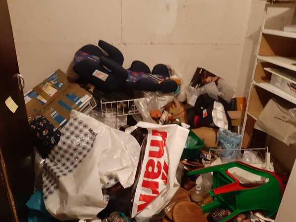 Chaotischer Abstellraum mit Kartons, Plastiktüten, Regalen und diversen Haushaltsgegenständen.